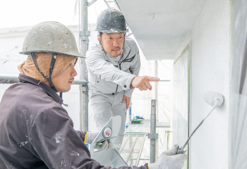 外壁塗装をしている作業員と、指差している代表の様子