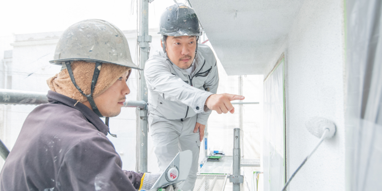 外壁を塗装している作業員と代表が外壁を指差している様子
